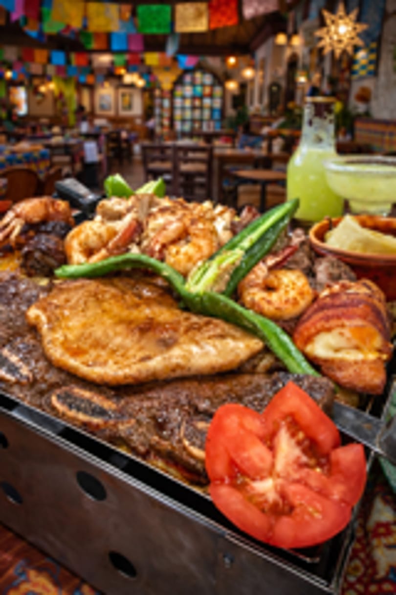 Grilled meats and shrimp fajitas with a tomato slice, in a vibrant Mexican restaurant setting.