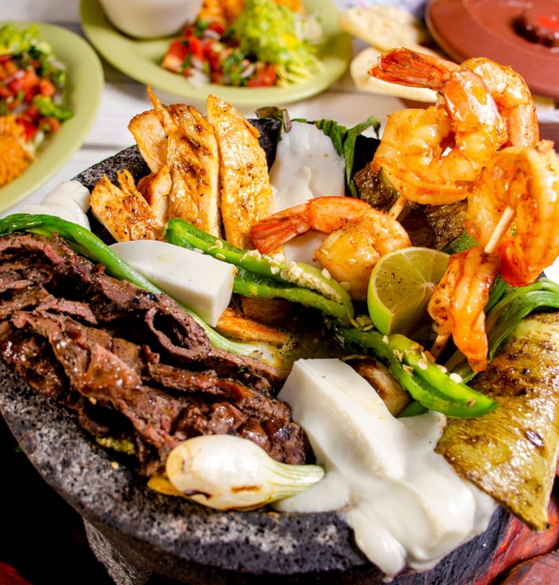 A molcajete filled with grilled chicken, shrimp, steak, peppers, onions, and cheese.
